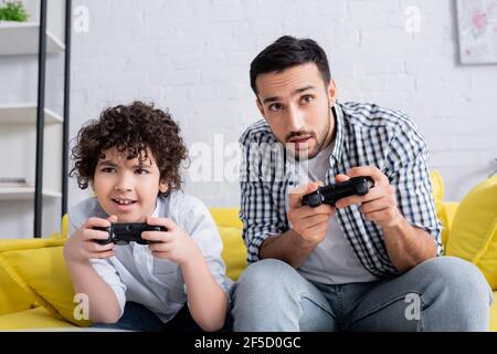 KYIV, UKRAINE - JANUARY 15, 2021: focused muslim father and son gaming together at home Stock Photo