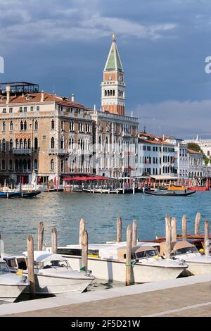 Taxi boats on calm water of Grand Canal im Venice. Old houses and tower of St Mark's Campanile by Canal Grande with dramatic sky in Venice, Italy. Stock Photo