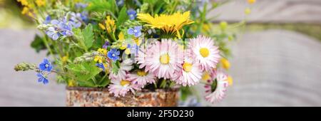 a bouquet of wildflowers of forget-me-nots, daisies and yellow dandelions in full bloom in a rusty rustic jar against a background of wooden planks in Stock Photo