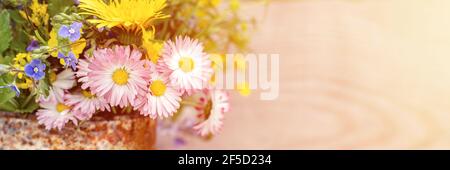 a bouquet of wildflowers of forget-me-nots, daisies and yellow dandelions in full bloom in a rusty rustic jar against a background of wooden planks in Stock Photo