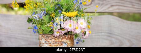 a bouquet of wildflowers of forget-me-nots, daisies and yellow dandelions in full bloom in a rusty rustic jar against a background of wooden planks in Stock Photo