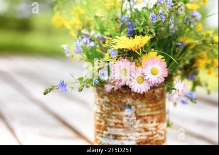 a bouquet of wildflowers of forget-me-nots, daisies and yellow dandelions in full bloom in a rusty rustic jar against a background of wooden planks in Stock Photo