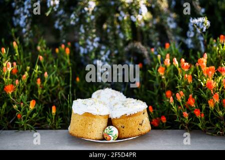 Plate with three Easter cakes covered with white glaze, in a flower bed. Stock Photo