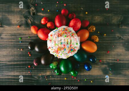 Easter cake sprinkled with multi-colored powder, with multi-colored painted chicken and Easter eggs on a wooden table. Stock Photo