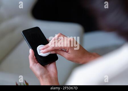 Midsection of mixed race businesswoman sitting disinfecting smartphone Stock Photo