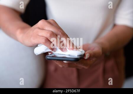 Midsection of mixed race businesswoman standing disinfecting smartphone Stock Photo