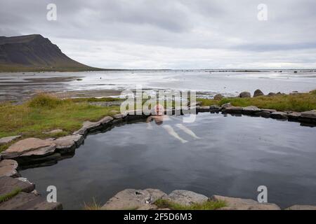man bathing in the Krosslaug natural geothermal pool directly on the coast, Iceland, Birkimelur Stock Photo