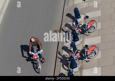 man on Santander hire bike rides past Santander hire bike know as boris bikes in dock stations Stock Photo