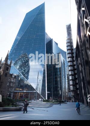 from left to right St Andrew Undershaft church, The Scalpel  skyscraper with Swiss Re reflected in windows,  Willis building, Lloyds insurance building, The Leadenhall building, with  pedestrian walking in quiet empty streets during coronavirus, Covid-19 pandemic Stock Photo