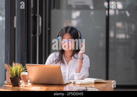 Asian girl with glasses look at laptop while doing homework making video call abroad using internet friend connection, Online learning education Stock Photo