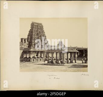 Conjivoram in Madras. View of a pillared kiosk in the courtyard of a temple complex in Kanchipuram. A gopura, or temple gate pyramid, sits to the left of the kiosk surrounded by a stone porch supported by carved pillars. The gopura features five tiers covered with ornately carved statues of Hindu deities. A group of men gather beneath the kiosk roof, sitting and standing, and face the camera. Painted stripes cover the base of the kiosk and the temple porch.. (Recto, mount) lower left, handwritten in pencil: 'A42.80 (Bou)' Lower center, handwritten in black ink: 'Conjivoram / in Madras' Lower r Stock Photo