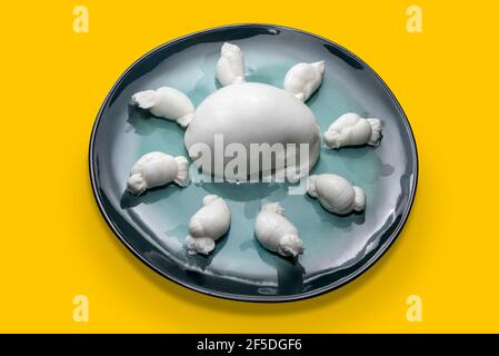Italian cheese mozzarella nodini with Buffalo mozzarella in aquamarine color glazed ceramic plate isolated on yellow background Stock Photo