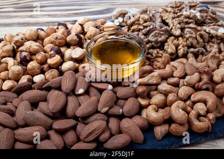 Various nuts sorted on stone plate with honey glass bowl. Mixed nuts on wooden table. Black stone plate on wooden background. Stock Photo