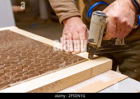 Carpenter puts together planks on the door frame using a pneumatic stapler in the carpentry workshop. Stock Photo