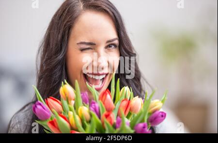 Happy dark haired woman blinking and holding a lovely bouquet full of tulips during national womens day. Stock Photo