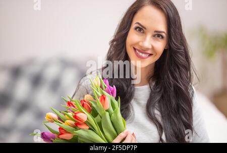 Beautiful dark haired woman holding in hands a lovely bouquet full of tulips during national womens day. Stock Photo