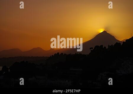 The sun setting behind the triangular peak of the Puig Campana, near Benidorm at the Costa Blanca, Spain Stock Photo