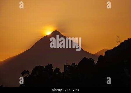 The sun setting behind the triangular peak of the Puig Campana, near Benidorm at the Costa Blanca, Spain Stock Photo