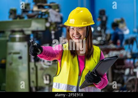 Portrait of Asian woman sales engineer checking the job list in paper over the photo blurred of lathe and milling machine background in metal factory, Stock Photo