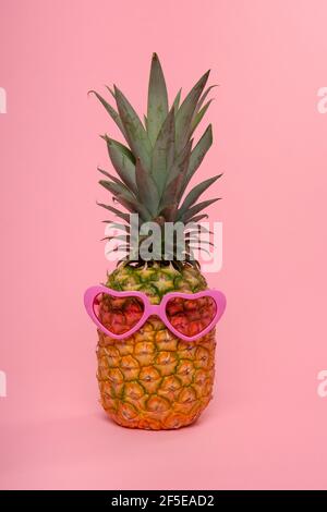 Funny pineapple with pink heart shaped glasses on a pink background Stock Photo