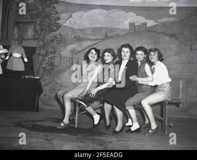 1956, historical, sitting on wooden bench on a stage, four young ladies in the costumes of their characters from the play, Jack & the Beanstalk, posing for a photo with a lady, perhaps their chaperon for the performance, England, UK. First published as an English fairy tale, 'The Story of Jack Spriggins and the Enchanted Bean' in 1734 and then in 1807 in 'The History of Jack and the Bean-Stalk' by Benjamin Tabert.  Fairy tales are ancient folklore, featuriing mythical creatures; elves, fairies, talking animals, witches and giants in magical stories that are far-fetched and not true, Stock Photo