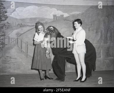 1956, on a stage, two young ladies in the costumes of their characters  with two people inside a cow costume in the pantomime, Jack and the Beanstalk. An ancient folk story, it was first published as an English fairy tale, 'The Story of Jack Spriggins and the Enchanted Bean' in 1734 and then in 1807 in 'The History of Jack and the Bean-Stalk' by Benjamin Tabert.  Fairy tales are ancient folklore, featuriing mythical creatures; elves, fairies, talking animals, witches and giants in magical stories that are far-fetched and not true and indeed could not possiblly be true. Stock Photo