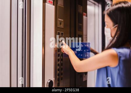 Woman in face mask pressing elevator button. Stock Photo