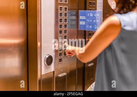 Woman in face mask pressing elevator button. Stock Photo