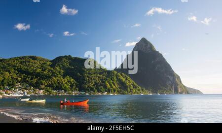 Soufriere, St Lucia. View from sandy beach across Soufriere Bay to Petit Piton, evening, fishermen in colourful boat at water's edge. Stock Photo