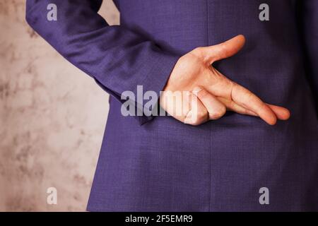Man in business suit holding crossed fingers behind his back. grey background Stock Photo
