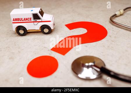 white ambulance on gray background next to red question mark and stethoscope. How long will road take. Have time to get to patient. Stock Photo