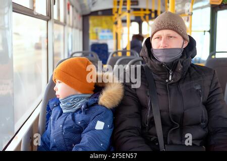 a man and a boy in a bus wearing medical masks. Dad and son in a public transport. bus ride during covid Stock Photo