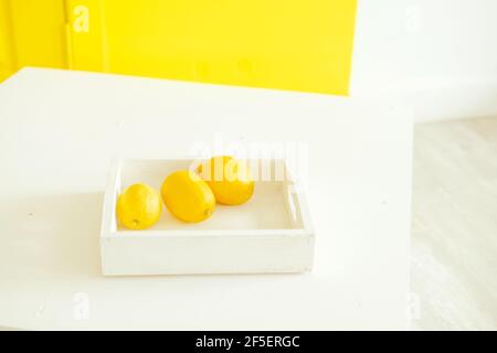 bright yellow lemons on a yellow background. Lemons on a white tray. Contrast photography with the color of the year. Stylish decor. Citrus fruits Stock Photo