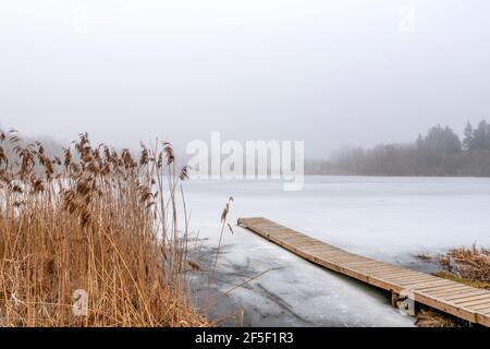 Wooden footbridge on lake with thick mist foggy air over frozen water.  Concepts: peaceful, mindfullness, secret, nature. Stock Photo