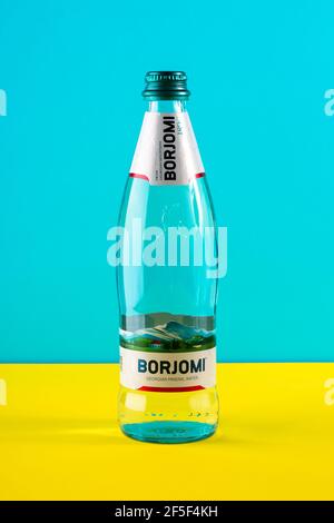 Borjomi glass bottle on yellow and blue paper background. Logo, brand of the company. Georgian mineral water, thirst quenching drink that eliminates h Stock Photo