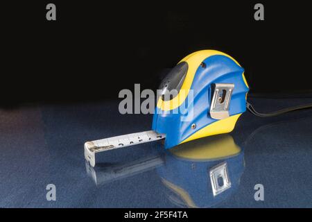 The construction tape measure is on the glass table. Tool on a black background Stock Photo