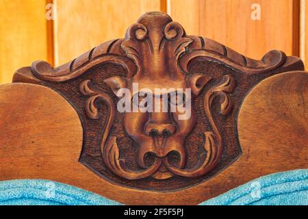 Close-up of carved gargoyle's head on backrest of blue velvet upholstered antique walnut wood chair in hallway on upstairs floor inside old 1807 house Stock Photo