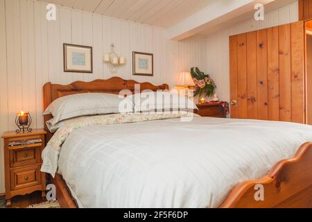 Queen size bed with solid pine wood-frame, headboard, footboard in upstairs master bedroom with white painted narrow wood plank walls inside old house Stock Photo