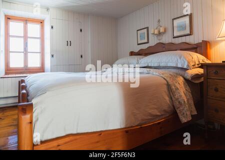 Queen size bed with solid pine wood-frame, headboard. footboard in upstairs master bedroom with white painted narrow wood plank walls inside old house Stock Photo