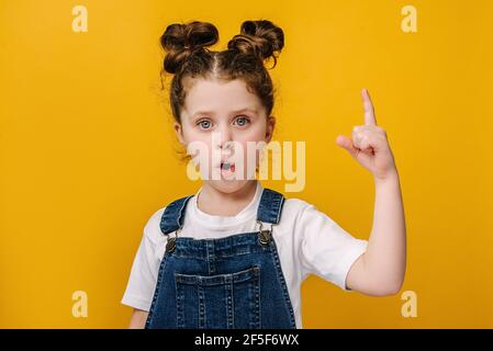 Close up portrait of funny little girl make gesture raises finger came up with creative plan feels excited with good idea, inspiration motivation Stock Photo