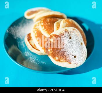 Pancakes with powdered sugar on a turquoise plate. Stock Photo