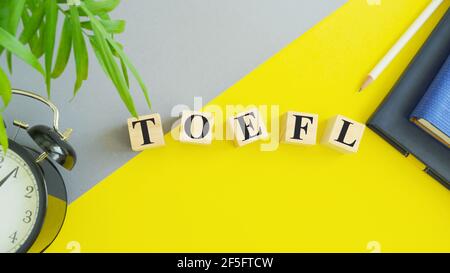 TOEFL - words from wooden blocks with letters, The Test of English as a Foreign Language, TOEFL concept, yellow background. Stock Photo