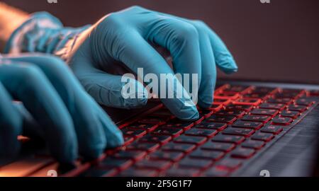 Hands in medical gloves type on a laptop keyboard in close-up. The concept of protection while working in quarantine Stock Photo