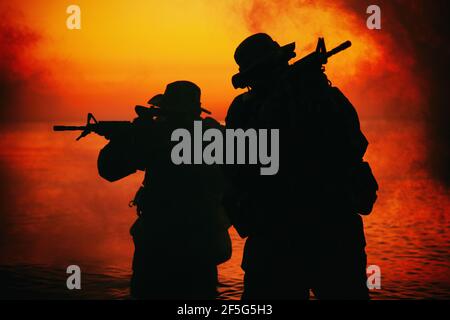 Commando soldiers walking in water, army special operations forces fighters sneaking in darkness, aiming assault rifles and observing shore during amphibious operation on coast at night or dawn Stock Photo