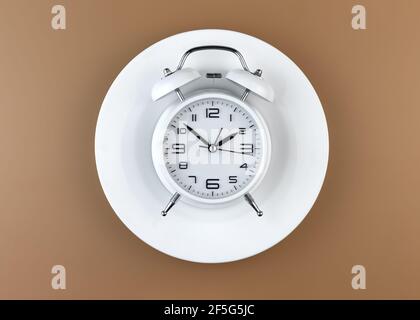 White alarm clock on an empty plate. Intermittent fasting concept.
