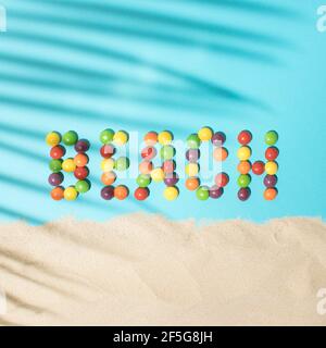 Beach word made from colored balls on a blue background with palm leaf shadow and sand. Tropical summer flat lay beach concept. Stock Photo