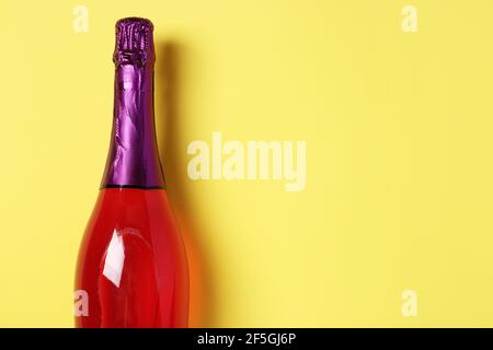 Sparkling pink champagne with glitter in bottle on yellow background. Space for text. Stock Photo