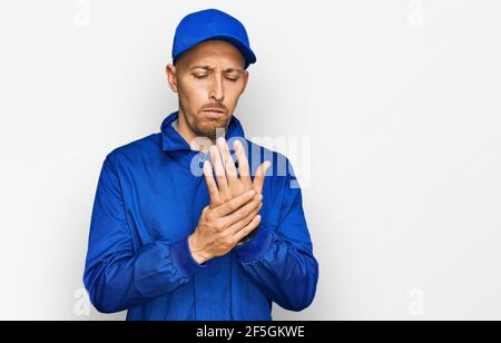 Bald man with beard wearing builder jumpsuit uniform suffering pain on hands and fingers, arthritis inflammation Stock Photo
