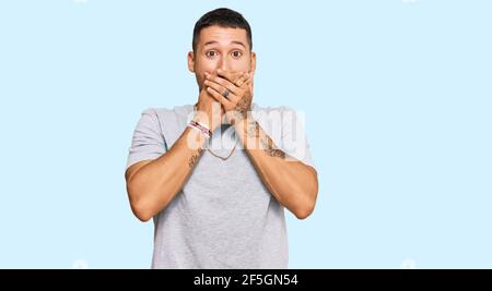 Handsome man with tattoos wearing 90s style shocked covering mouth with hands for mistake. secret concept. Stock Photo