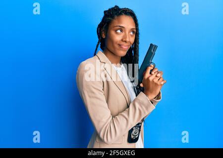 African american police woman holding gun smiling looking to the side and staring away thinking. Stock Photo